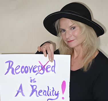 Carolyn Costin holding a sign that reads Recovered is a Reality